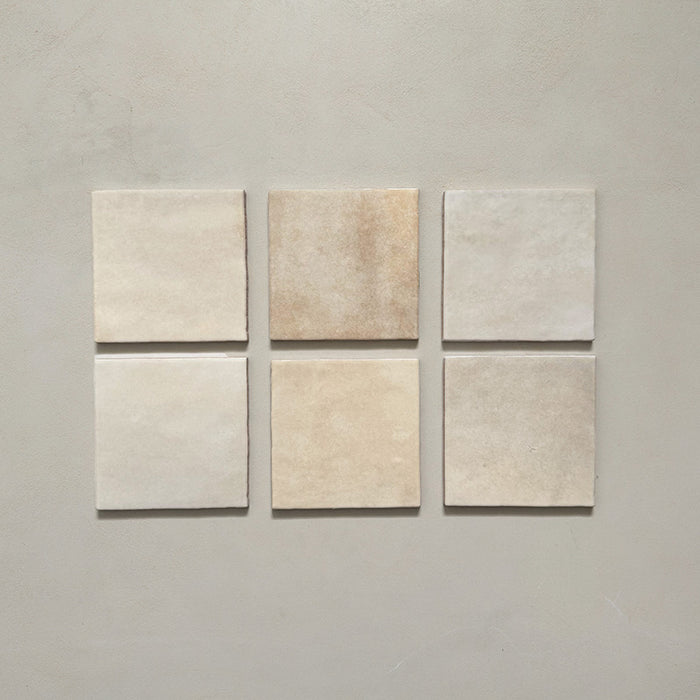 Vista cenital de azulejos de pared cerámicos Zellij Ocre Cuadrado 13,2 × 13,2 cm de estilo marroquí, presentados como piezas individuales, destacando la variación tonal suave, los bordes ligeramente irregulares y el acabado brillante artesanal en tonos neutros cálidos sobre un fondo liso.
