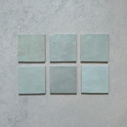 Vista cenital de azulejos de pared cerámicos Zellij Aqua Cuadrado 13,2 × 13,2 cm de estilo marroquí, presentados como piezas individuales, mostrando la suave variación tonal en azul, el acabado brillante artesanal y los bordes sutilmente irregulares para un aspecto auténtico y lleno de carácter.