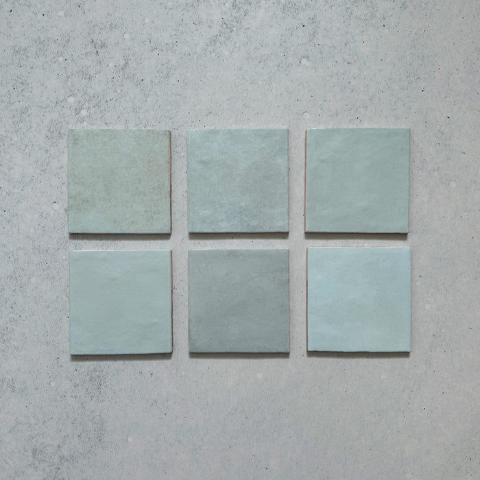 Vista cenital de azulejos de pared cerámicos Zellij Aqua Cuadrado 13,2 × 13,2 cm de estilo marroquí, presentados como piezas individuales, mostrando la suave variación tonal en azul, el acabado brillante artesanal y los bordes sutilmente irregulares para un aspecto auténtico y lleno de carácter.