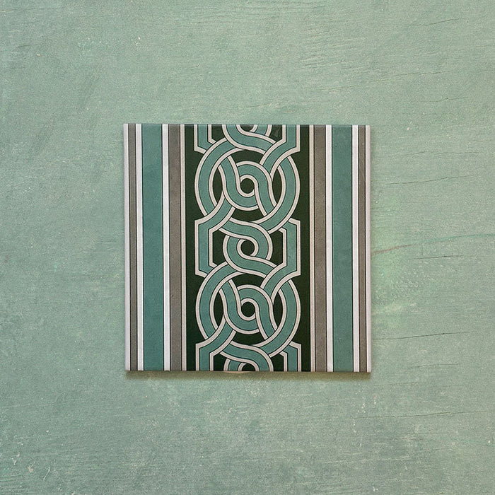 Single Europa Toulouse 20x20cm Victorian Moroccan style border tile displayed against a textured green background, featuring a decorative interlocking geometric pattern in green, grey and cream tones.