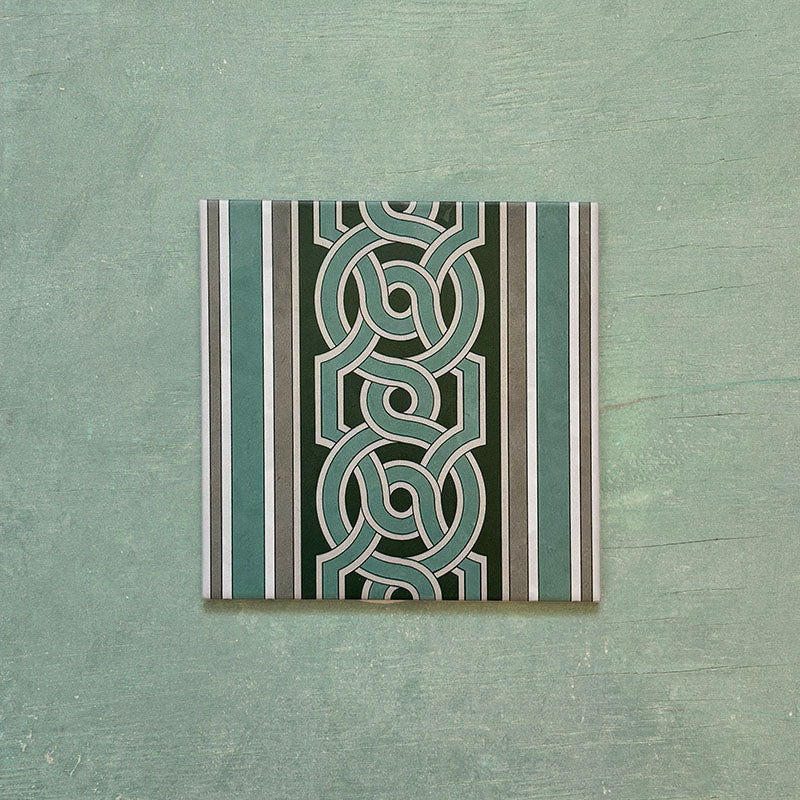 Single Europa Toulouse 20x20cm Victorian Moroccan style border tile displayed against a textured green background, featuring a decorative interlocking geometric pattern in green, grey and cream tones.