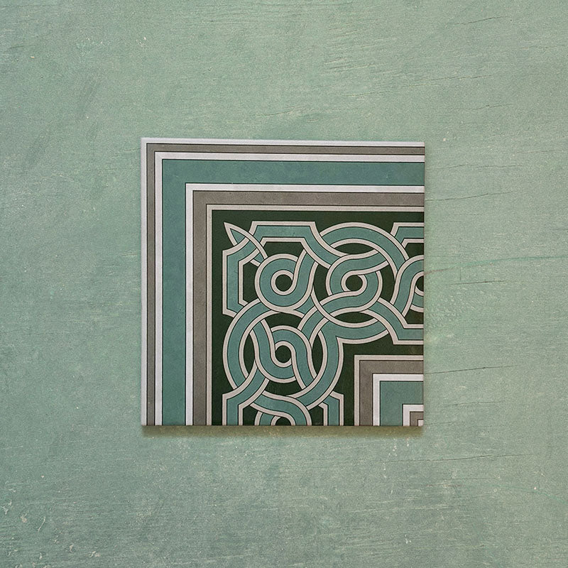 Single Europa Toulouse Corner 20x20cm Victorian Moroccan style tile displayed against a textured green background, featuring a decorative corner border design in green, grey and cream tones.