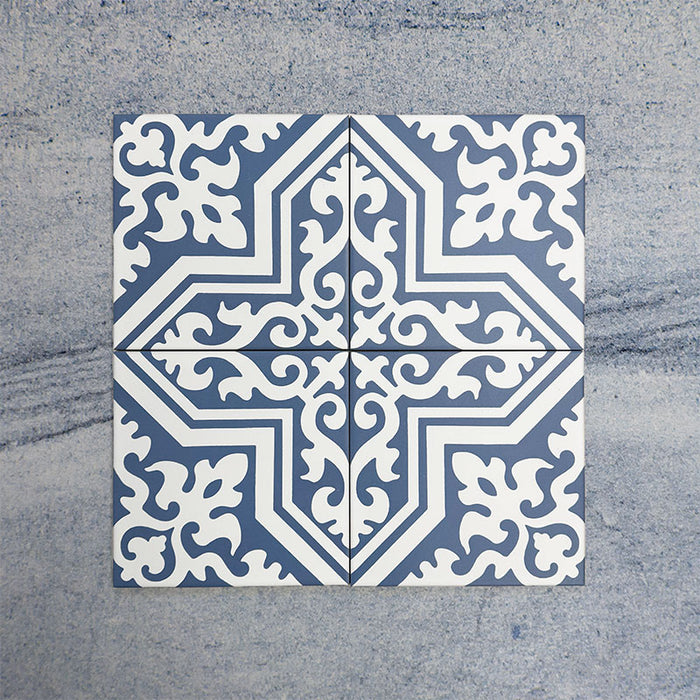 Cuatro baldosas Europa Trondheim Blue 20 × 20 cm de estilo Victoriano Marroquí colocadas juntas para mostrar el patrón decorativo repetitivo en tonos azul y blanco, sobre un fondo gris texturizado.