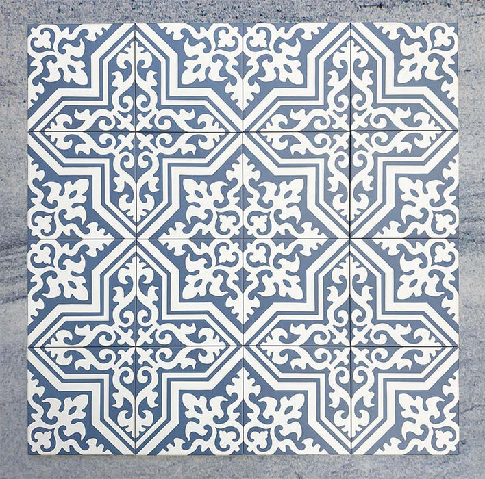 Grupo de baldosas Europa Trondheim Blue 20 × 20 cm de estilo Victoriano Marroquí dispuestas juntas para mostrar el patrón decorativo repetitivo en tonos azul y blanco, sobre un fondo gris texturizado.