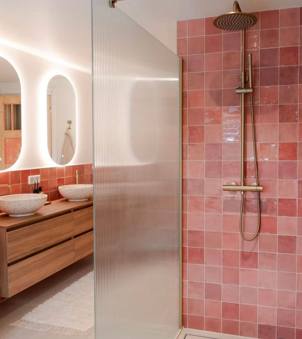 Baño contemporáneo con azulejos de pared cerámicos Zellij Pink Square 13,2 × 13,2 cm de estilo marroquí, mostrando una suave variación tonal en rosa y una textura brillante de aspecto artesanal, combinados con grifería de ducha de latón, vidrio acanalado y mobiliario de madera cálida.