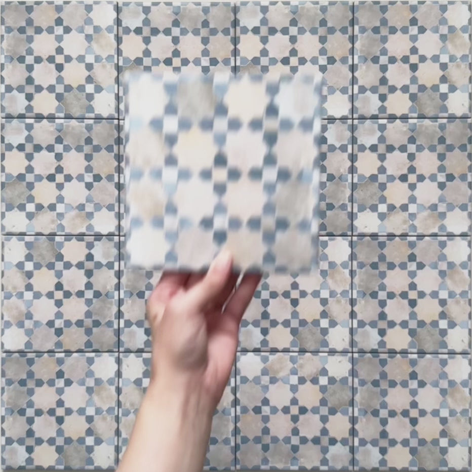 Vídeo breve de los azulejos de estilo marroquí Bedouin Mequinez Azul 15x15 cm, destacando su intrincado patrón geométrico en azul suave, crema y topo, con acabado efecto pintado a mano y ligera variación superficial.